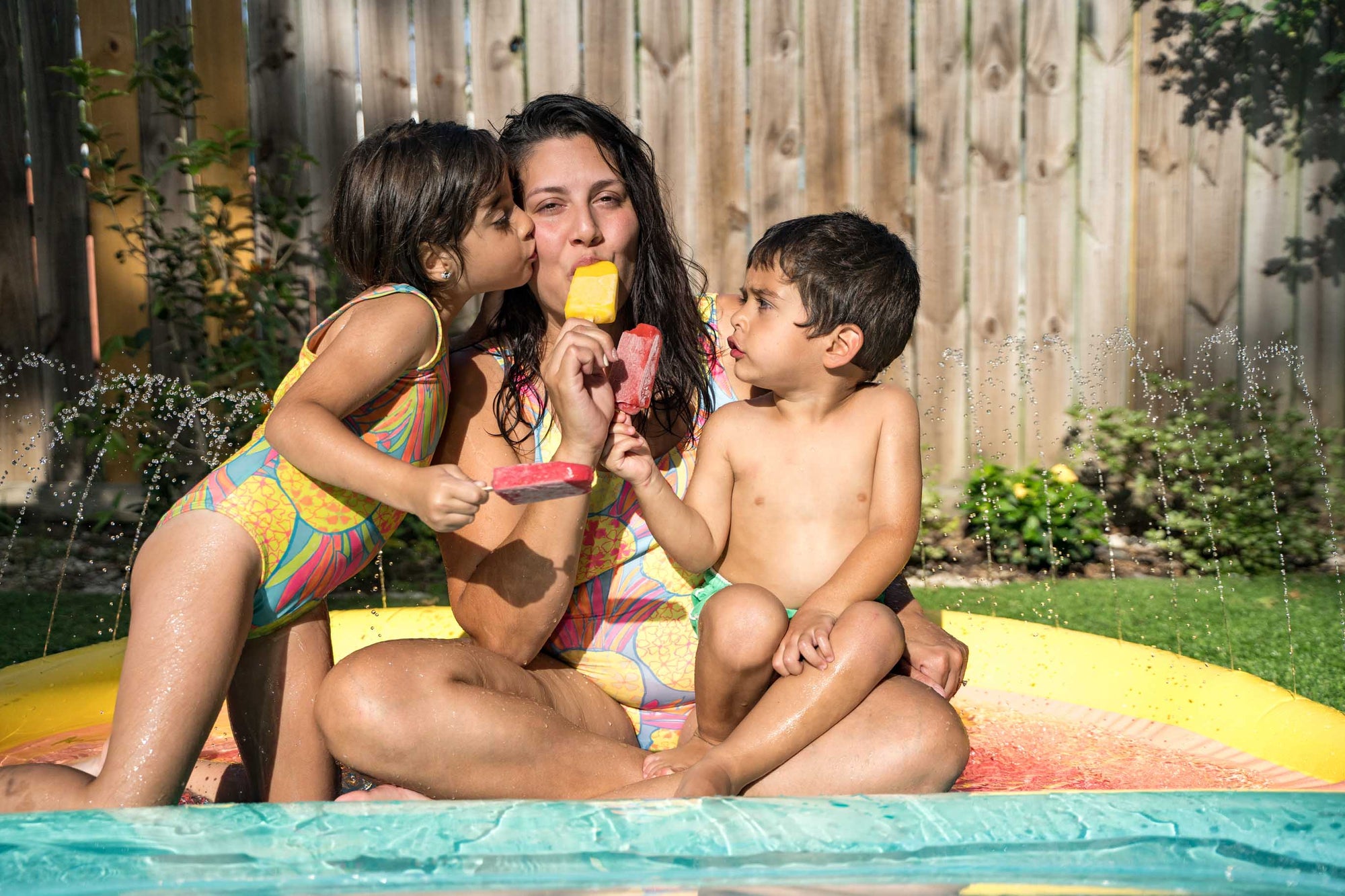 Mom, daughter and son wearing a pineapples swimsuit and having All-Natural Ice Pops in a backyard water party 