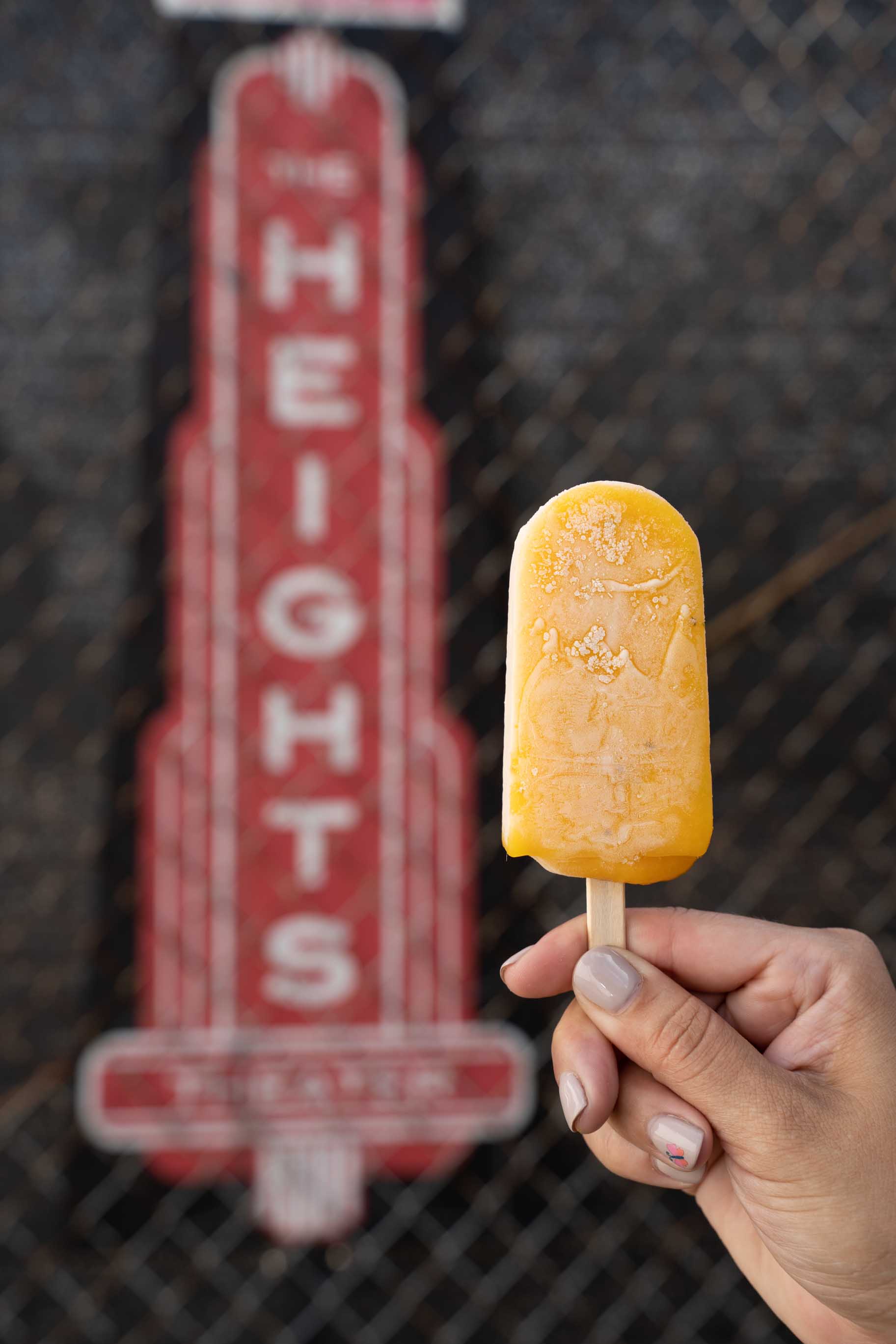 Mango artisan popsicle held by woman hand in front of The Heights theater logo.