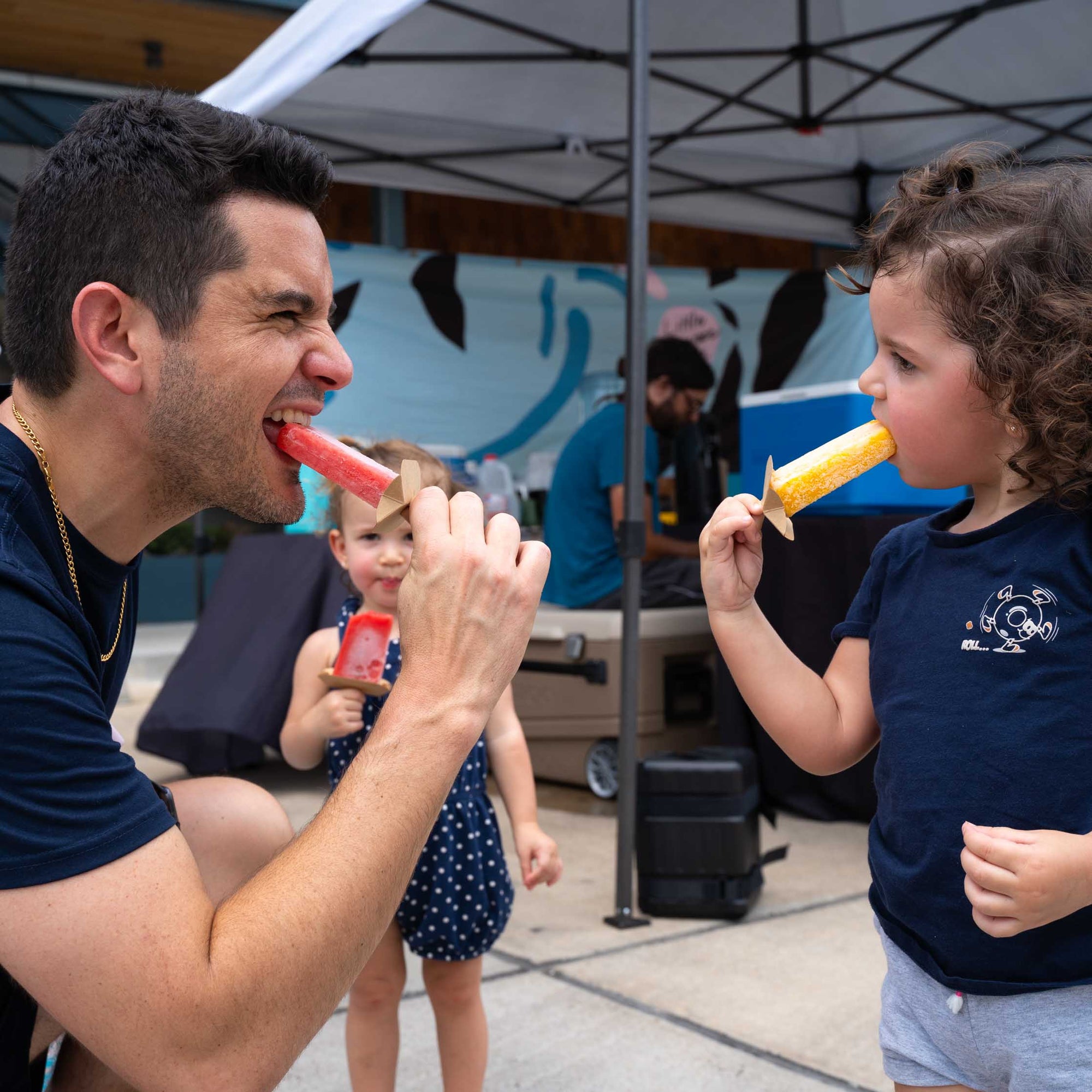 Dad and daughter having a natural fruit ice pop at a carnival.