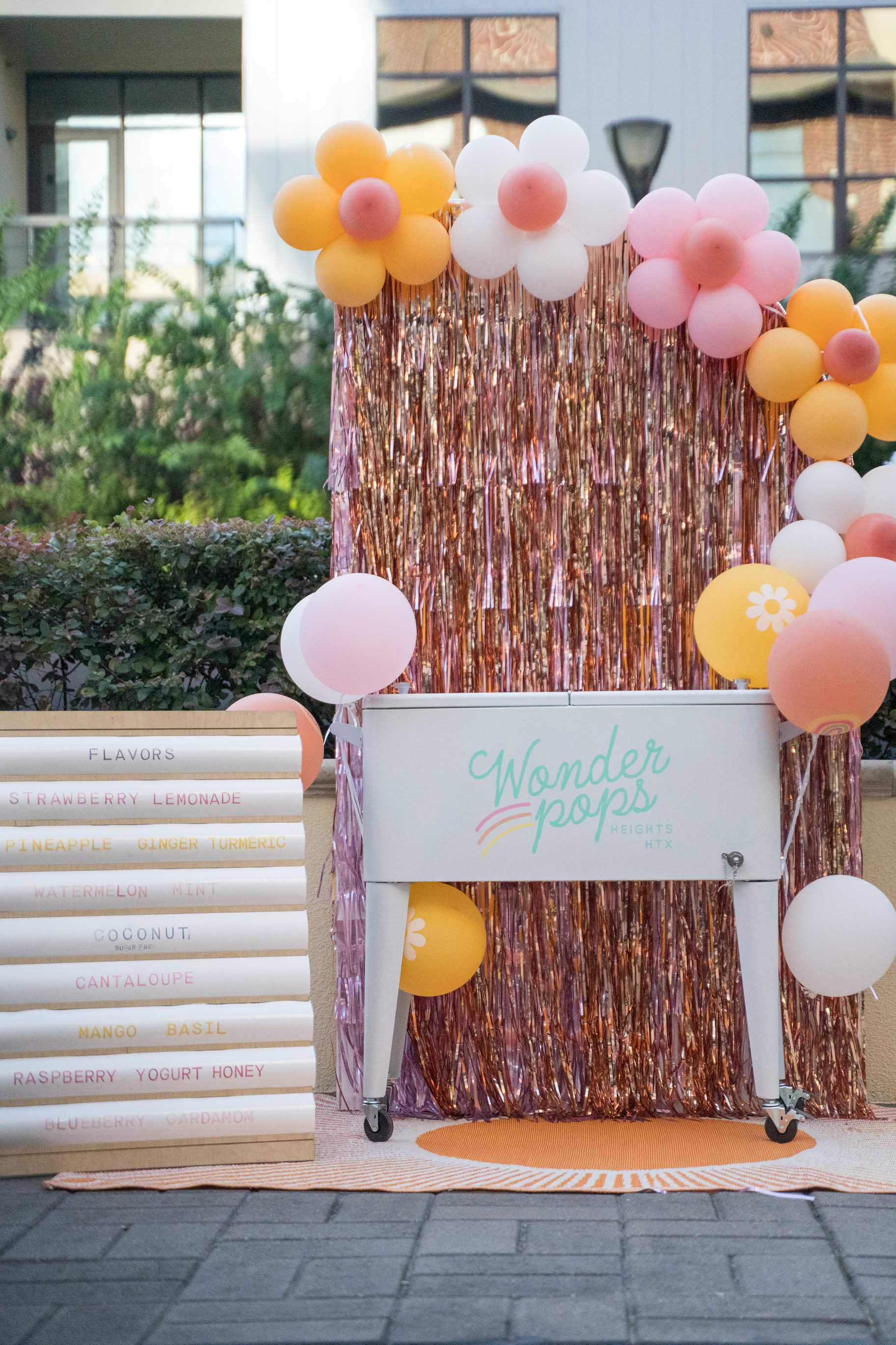 Vintage White cooler cart with custom flavor menu and custom vintage backdroop and flower balloons.