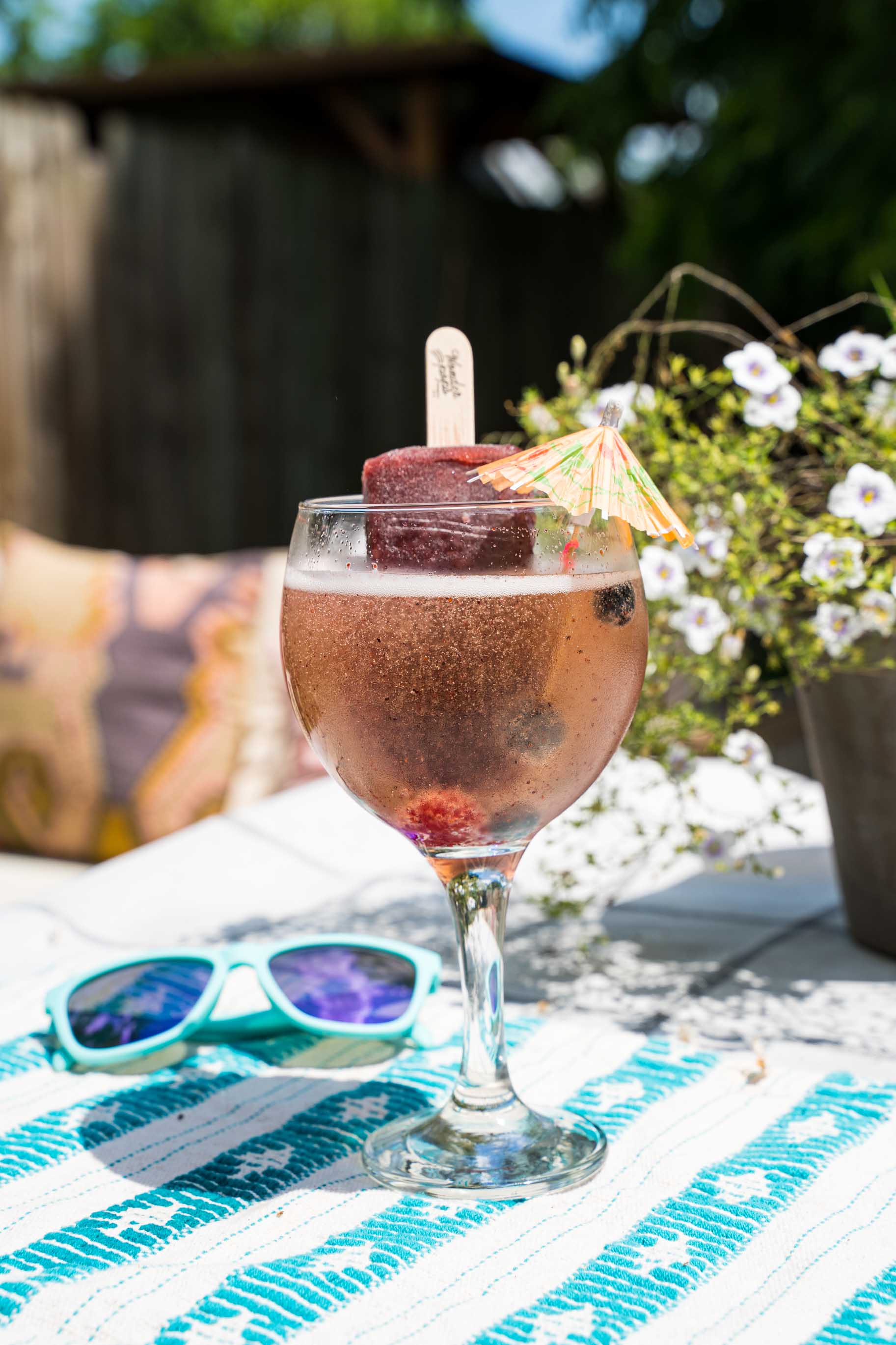 Artisan ice pop dipped in a mimosa drink glass on backyard table with flowers and sunglass.