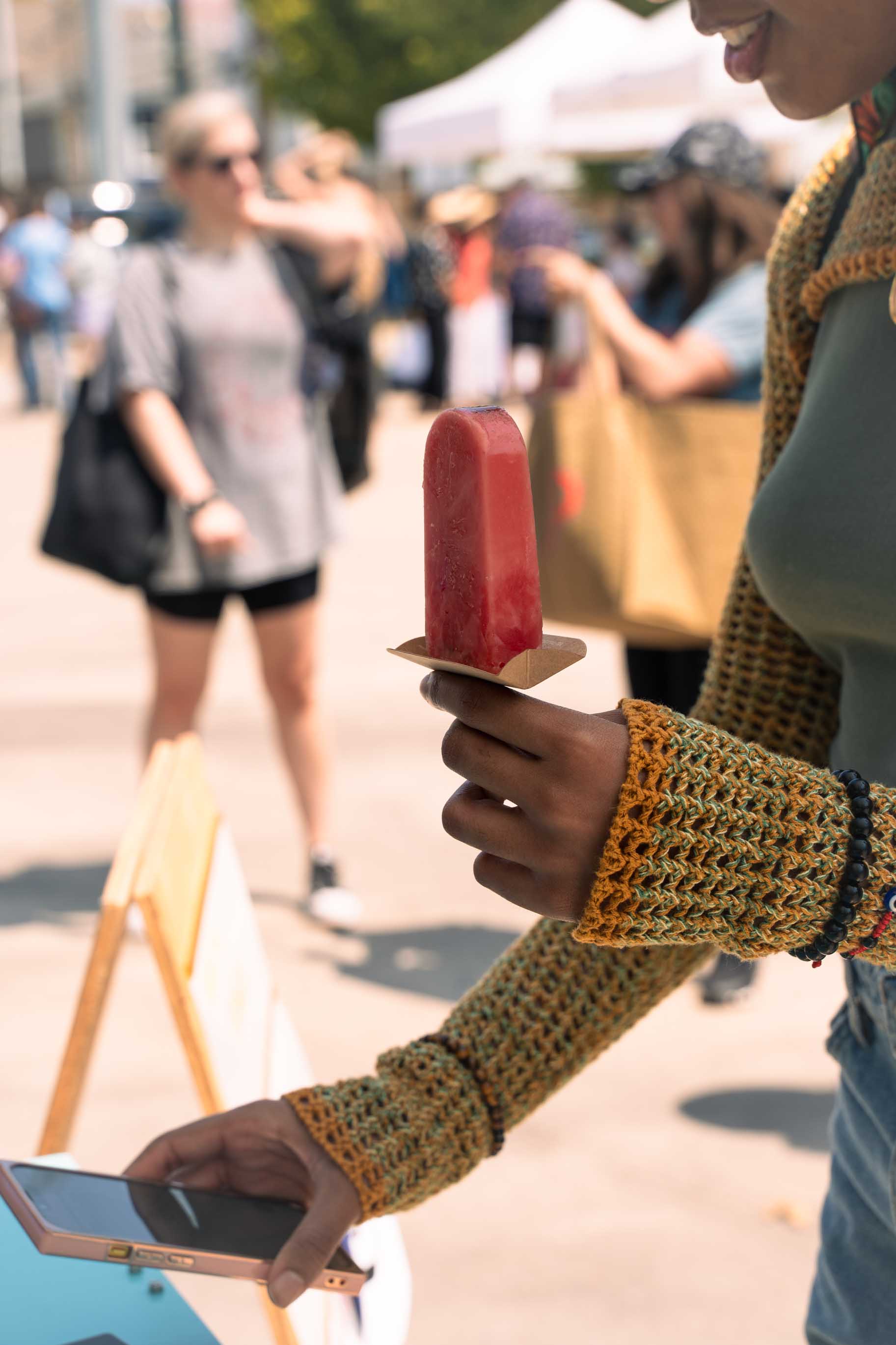 Afroamerican woman holding a vegan all natural ice popsicle at a private event. Paying with mobile wallet. 