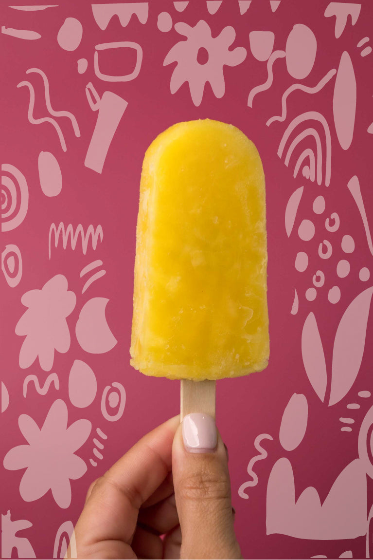 Pineapple ice pop held by a woman hand. Background with flower doodles.