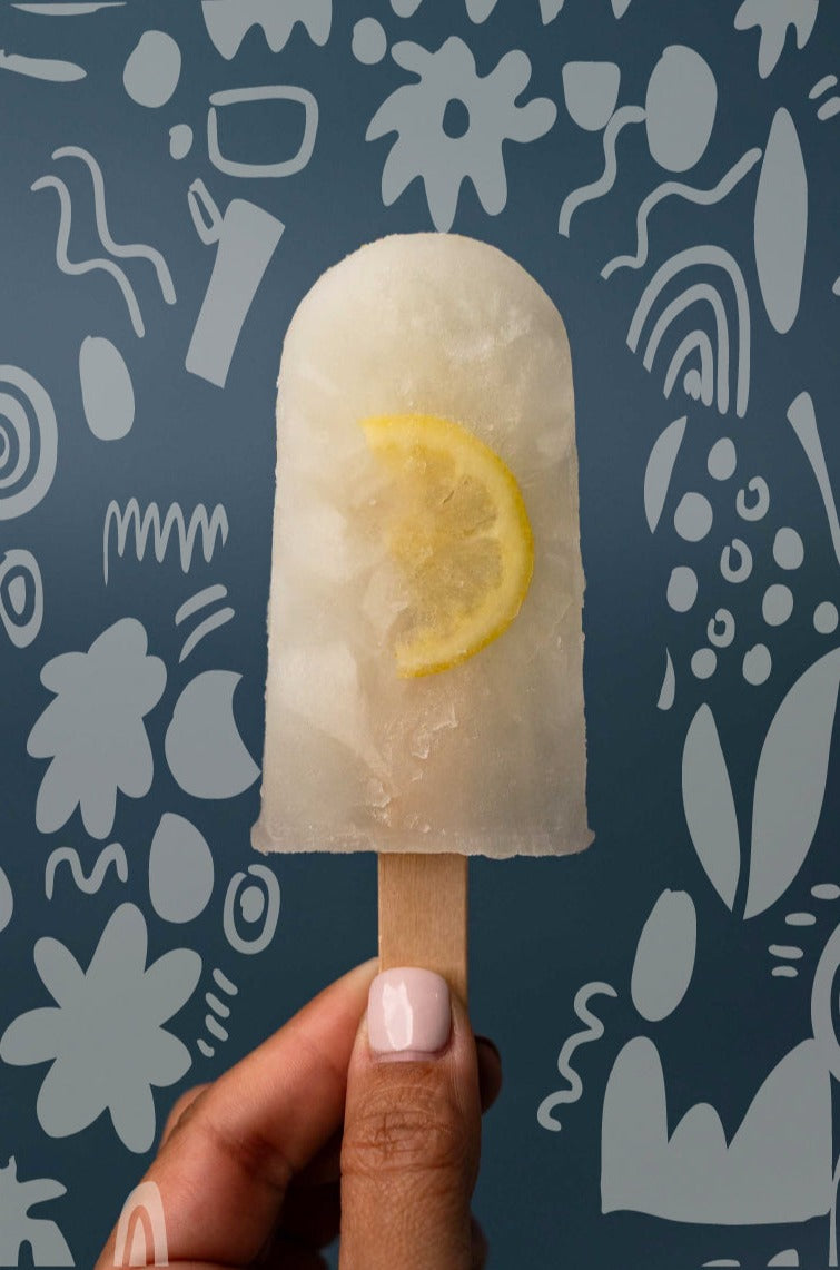 Lemonade natural ice pop held by a woman hand. Background with flower doodles.