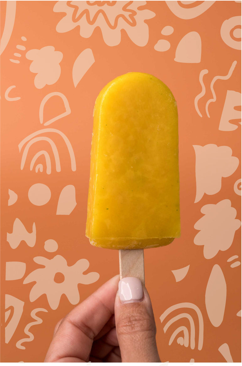 Mango vegan ice pop held by a woman hand. Background with flower doodles.