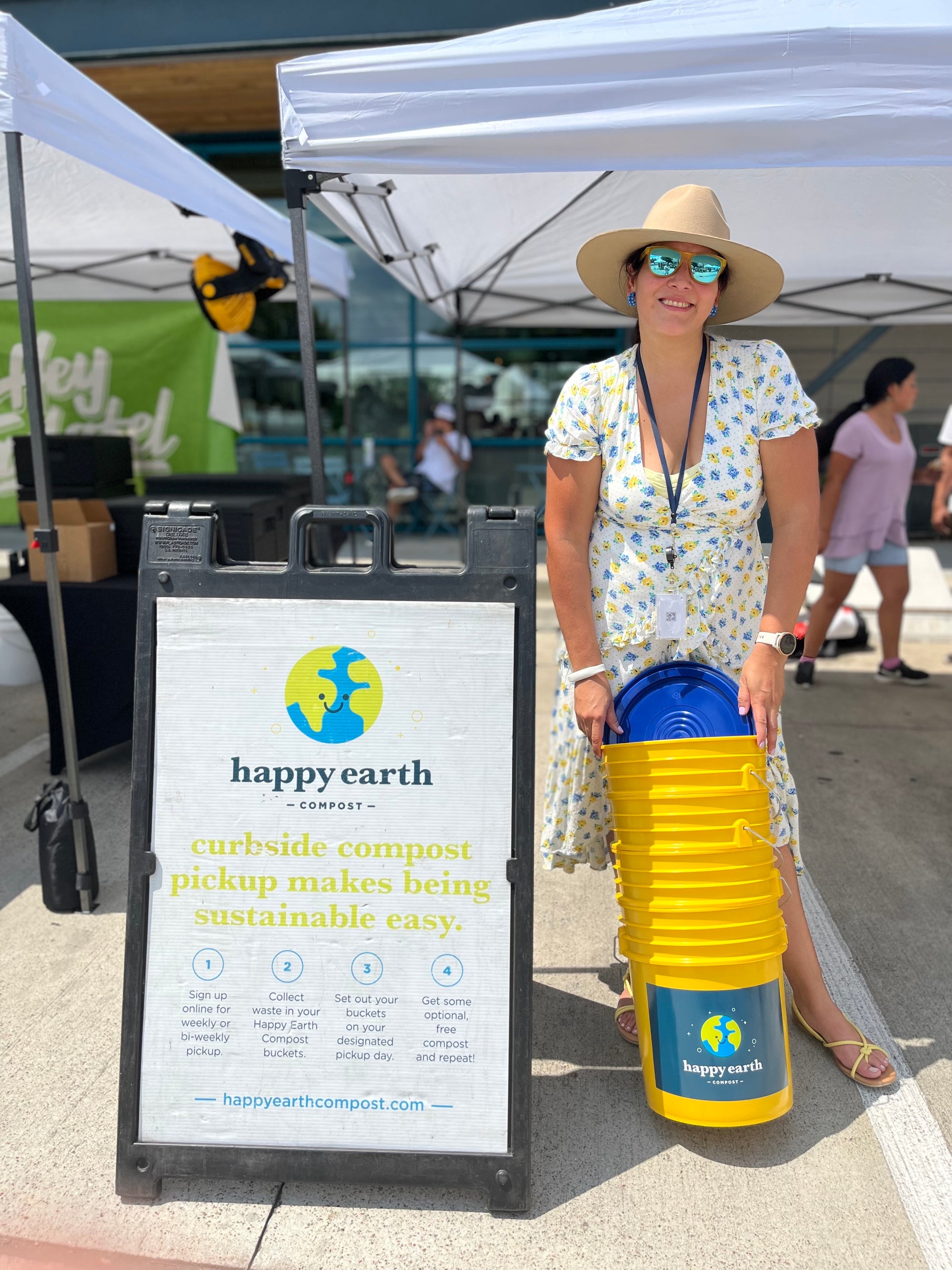 Woman holding compost buckets next to sign promoting environmental sustainability